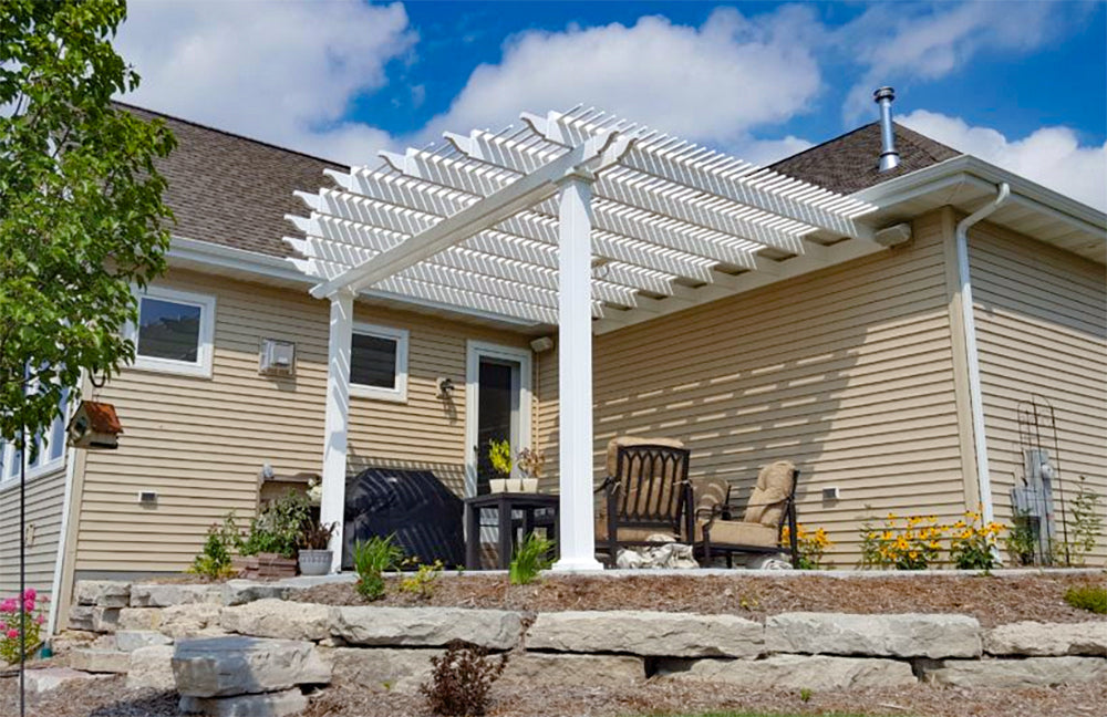 white pergola attached to a house on an elevated cement platform with outdoor furniture