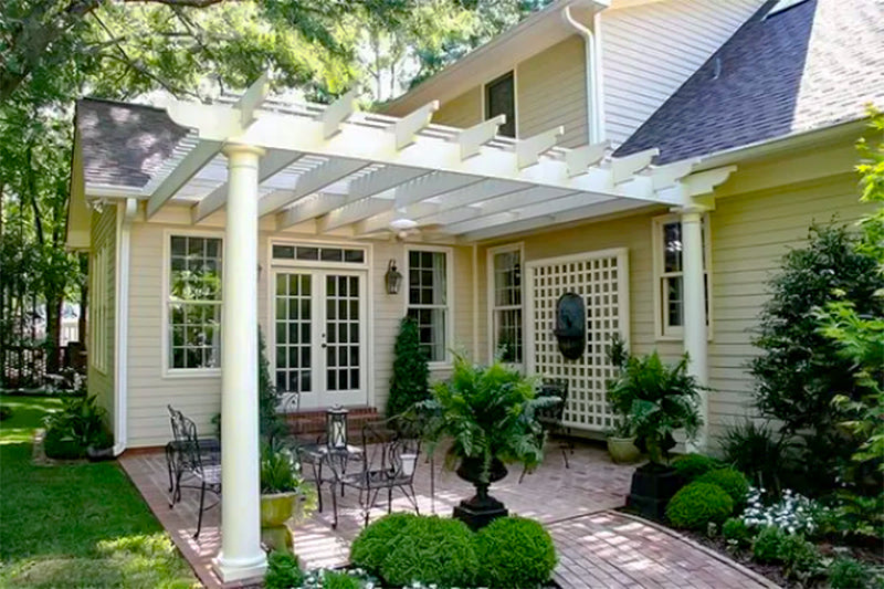 white pergola attached to a house with outdoor furniture on a paver