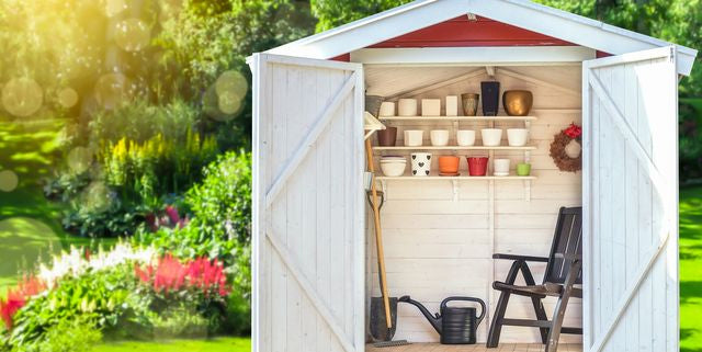 wood shed painted white with doors open and gardening tools inside