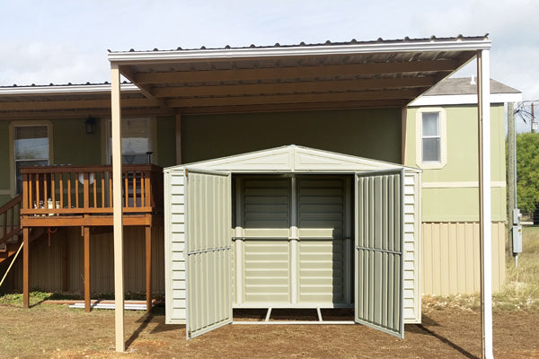 Duramax vinyl shed positioned adjacent to a residential home, featuring open doors under a protective awning, demonstrating how it blends seamlessly with home exteriors and provides accessible storage.