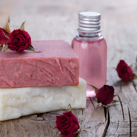 2 bars of soap next to rose buds and a bottle of oil