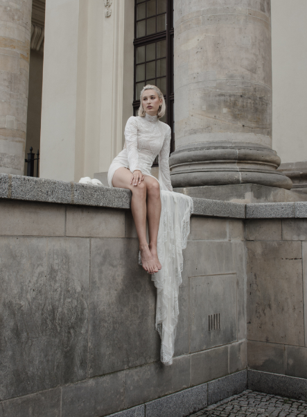 Braut sitzt in Brautkleid auf einer Mauer und trägt Brautschmuck von Maren Jewellery