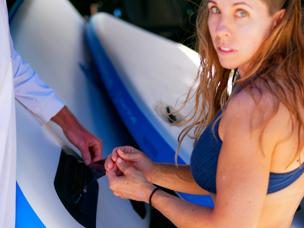 Girl placing a fin on an inflatable SUP board