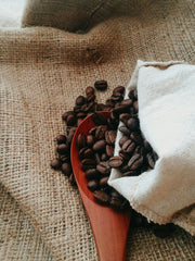 Bag of coffee beans spilling onto a red wooden spoon