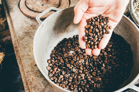 Hand holding coffee beans over bowl.