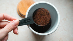 Measuring spoon scooping coffee grounds from a ceramic container