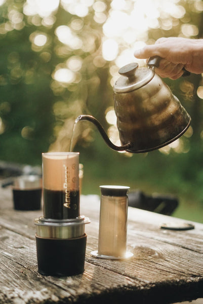 Pouring hot water into an AeroPress coffee maker outdoors.