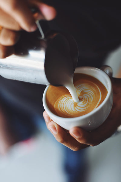 Hands pouring latte art into cup with low-acid coffee.
