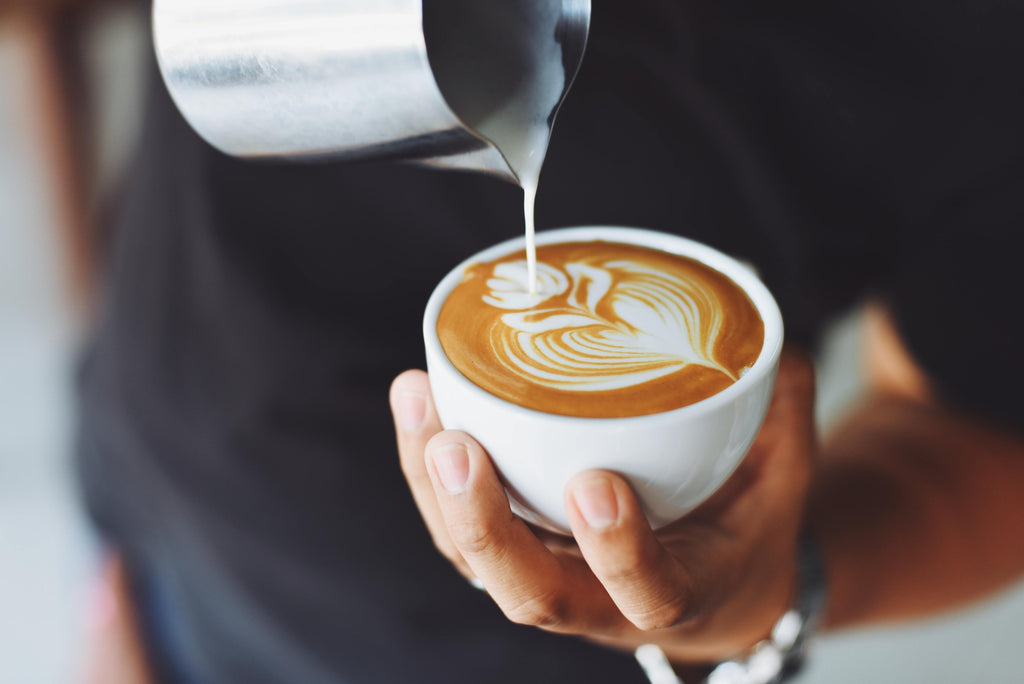 Barista hand-pouring latte art into a white mug.