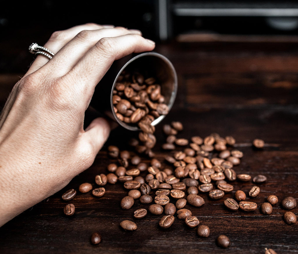 Hand pouring out coffee beans on a dark wooden surface.