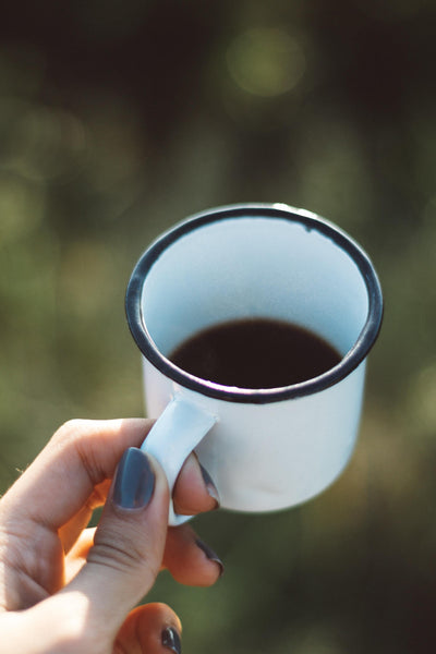 Female hand holding a cup of coffee against forest background.