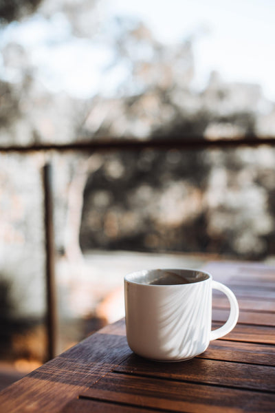 Coffee cup on a wooden table with a lush, out of focus background.