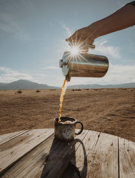 Pouring coffee into a cup from a percolator outdoors.