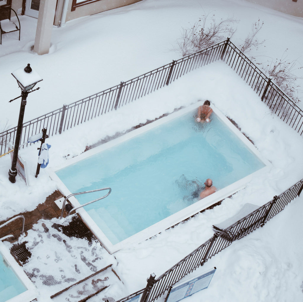 Couple swimming in pool outdoors during winter.