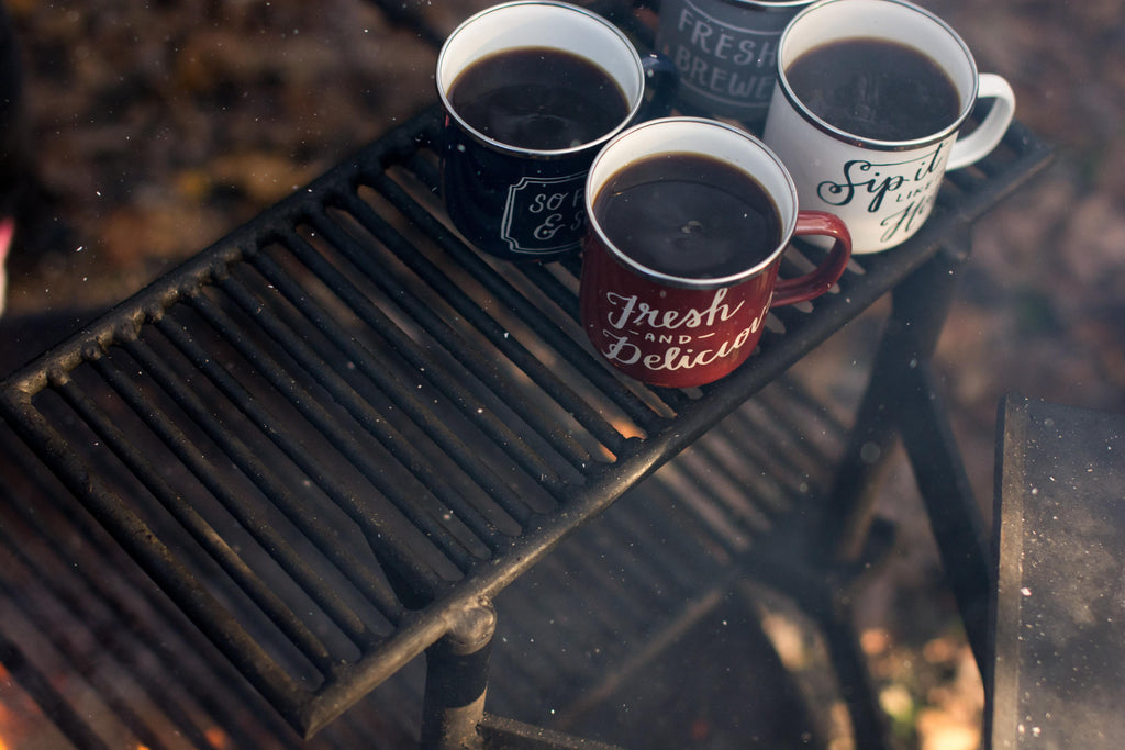Steaming cups of coffee on a metal grid stand outdoors. 