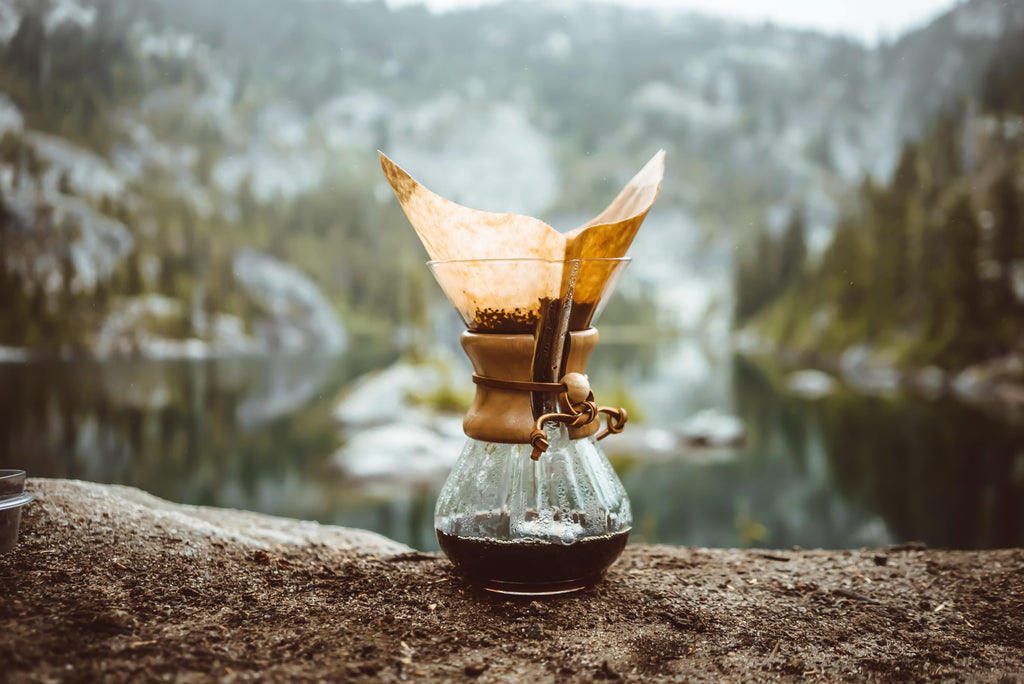 Chemex coffee maker against a backdrop of a mountain lake.