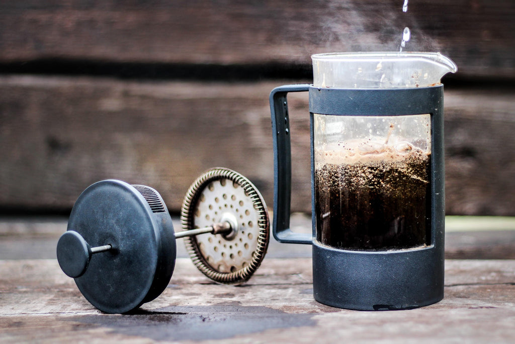 A French Press Coffee Brewer against a wooden backdrop.