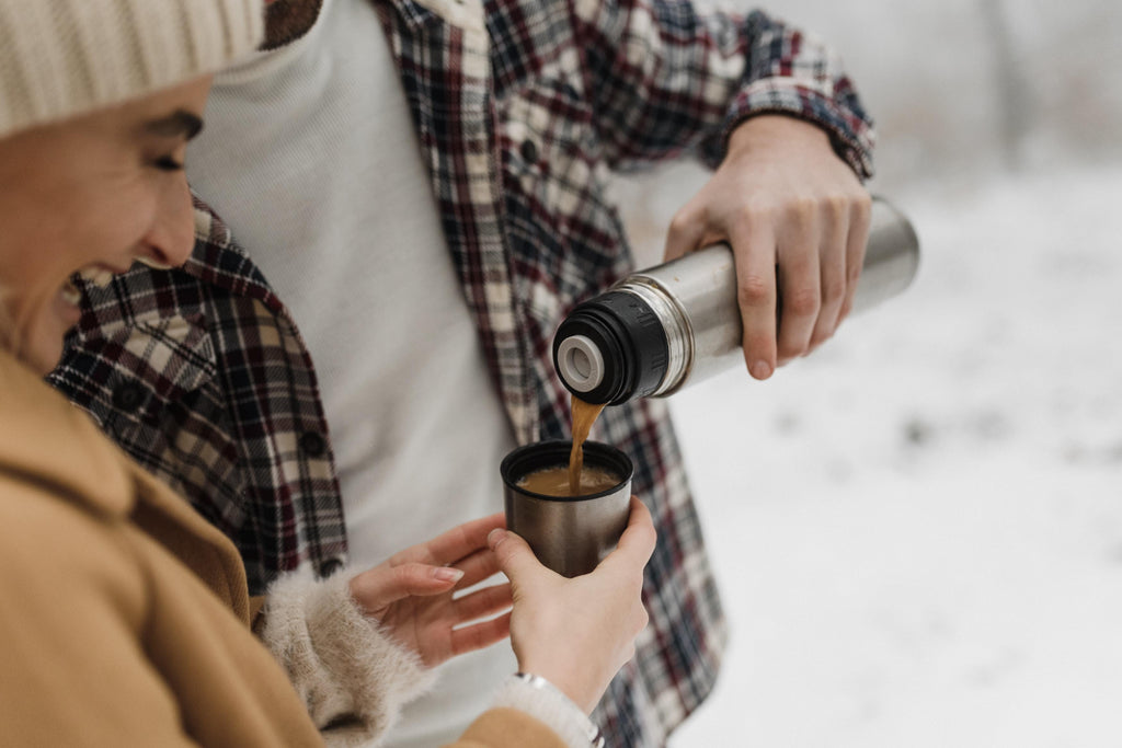 Two happy friends pouring coffee from a thermos in winter.