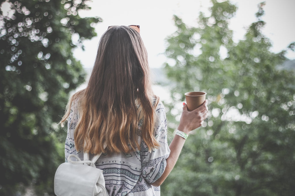 Young girl with her back turned, holding a single-use coffee cup.