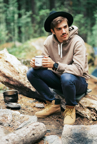Young man drinking coffee by a campsite in a forest.
