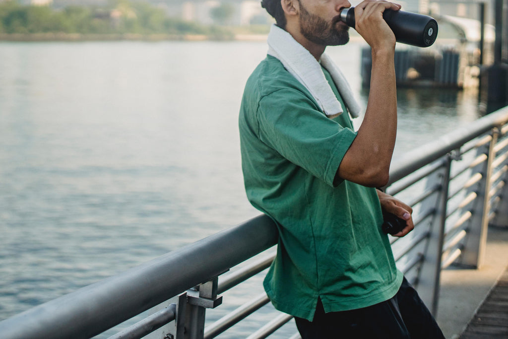 Man leaning against railing after workout, drinking water. 