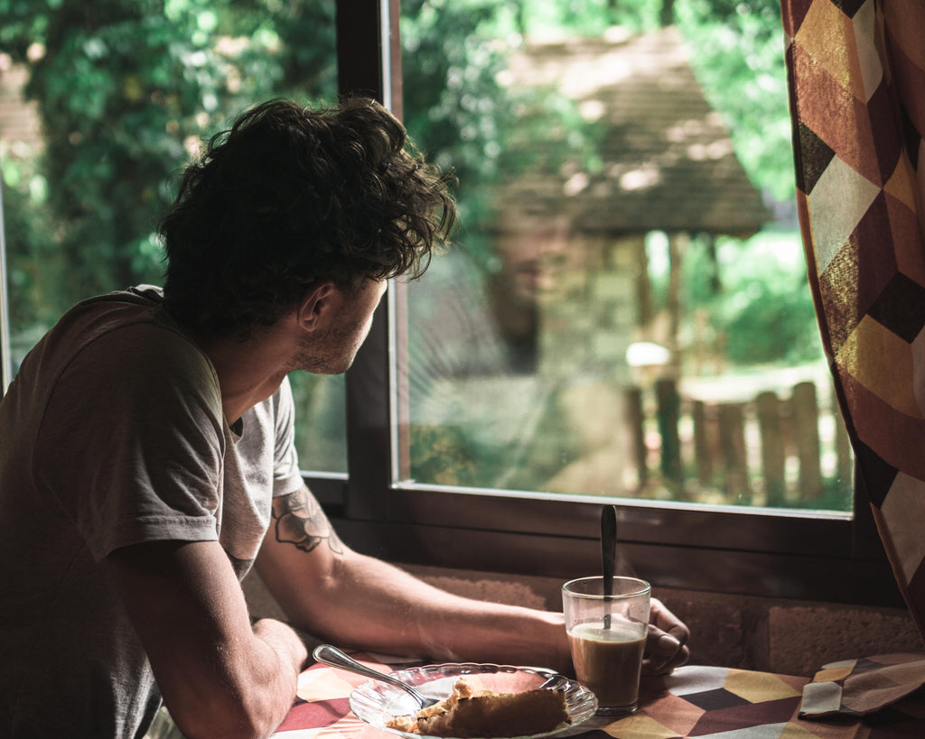 Young man staring distantly out the window while eating breakfast.