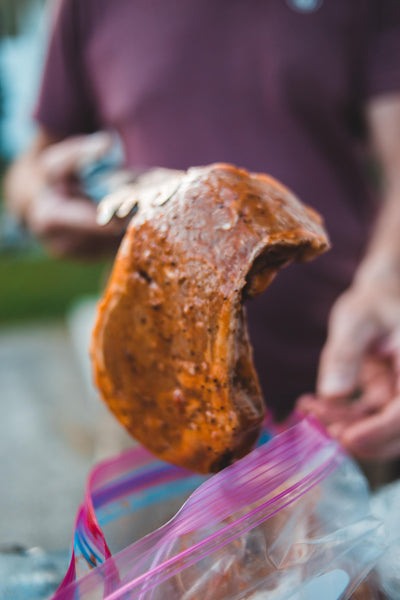 Man holding up uncooked meat covered in marinade.