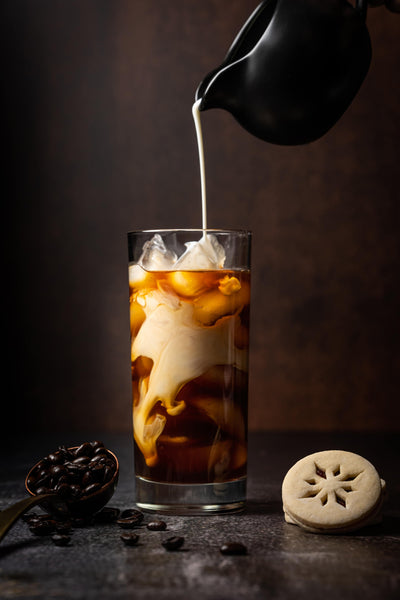 Milk pouring into a tall glass with cold brew coffee.