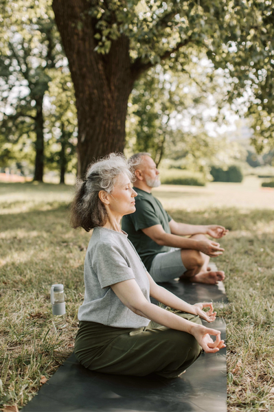 Older couple in cross-legged positions in a park, doing breathwork.