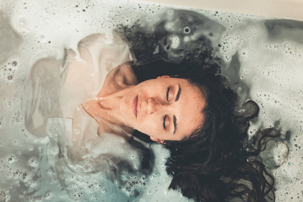 Woman floating in bath, eyes closed and relaxing.