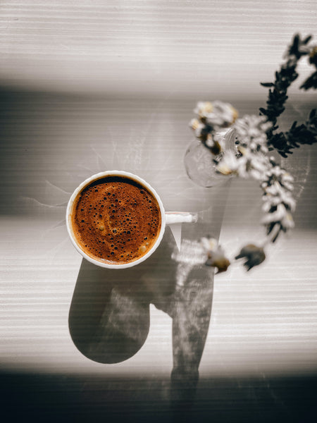 Cup of freshly brewed coffee on white table with flowers.