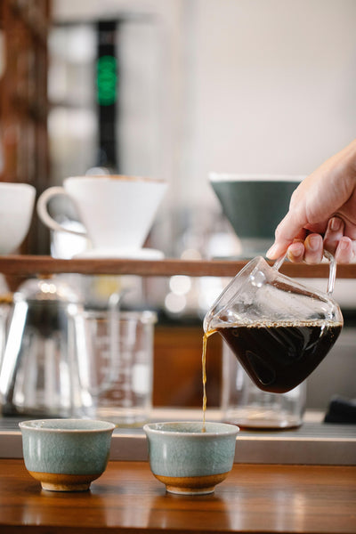 Pouring coffee into two small cups on a table.