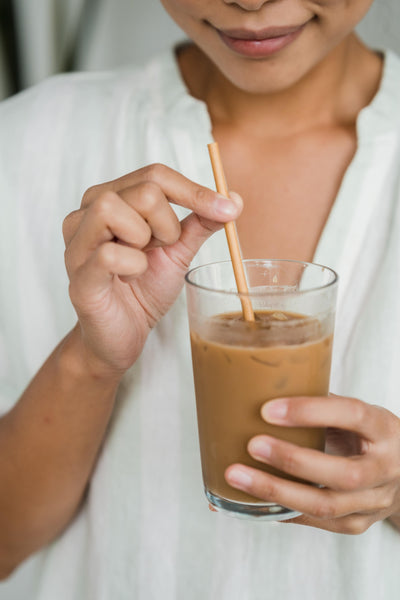 Woman smiling while stirring a glass of cold brew coffee in her hand.