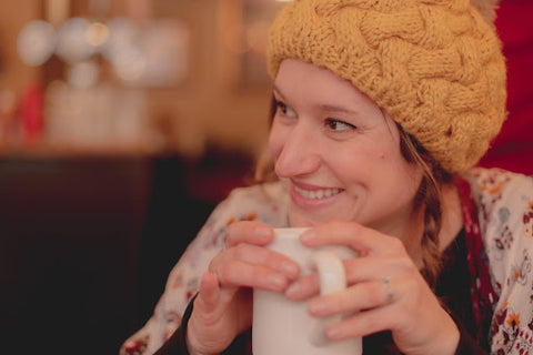 A young woman smiles with a cup of coffee.