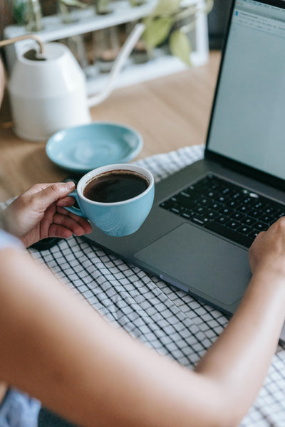 Person working in front of a computer with a cup of coffee.