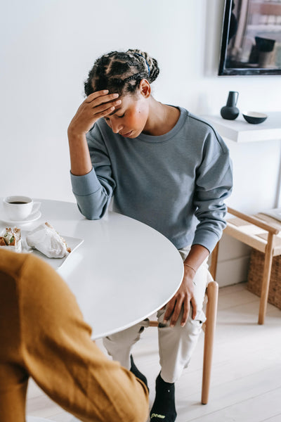 Woman holding her head in pain at a kitchen table.