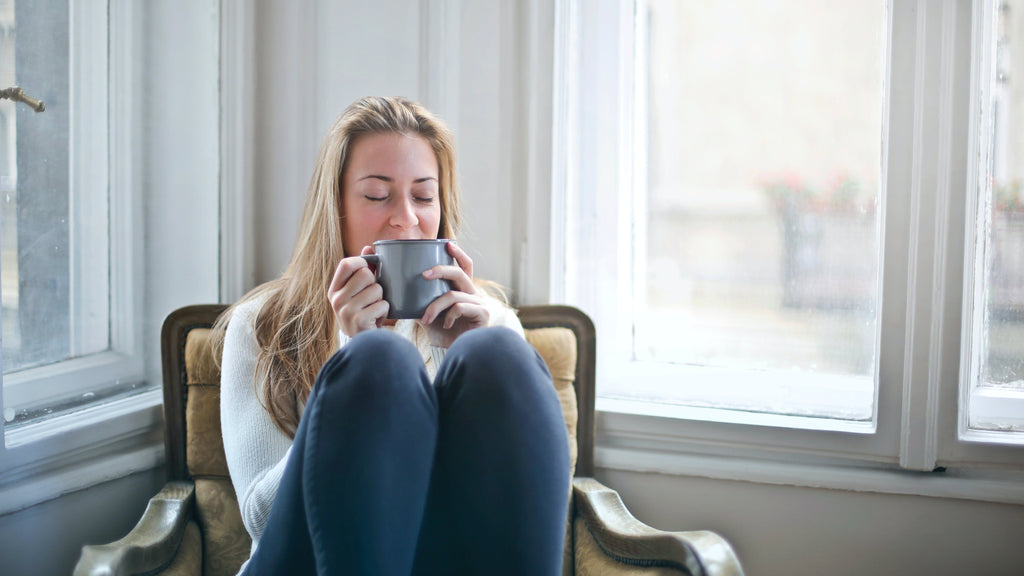 Young woman calm and happy, with a cup of coffee in a chair by the window.