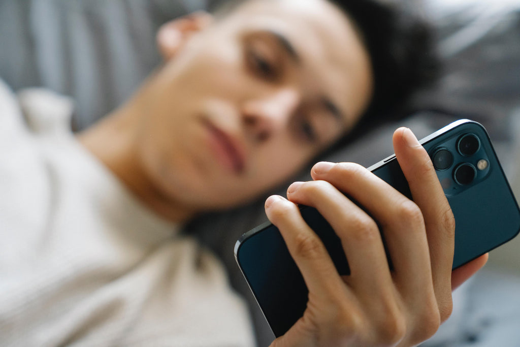 Young man scrolling phone in bed.