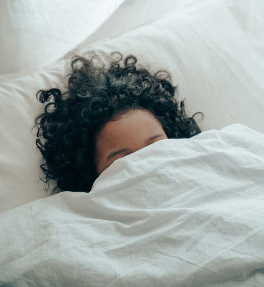 A woman sleeping with her face covered by a blanket.