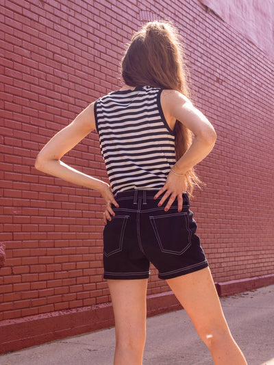 A model wearing a miter print black and scoop neck tank with a contrasting scoop neck in black. The model is wearing a pair of black shorts with white contrasting stitches. With black platform sandals.