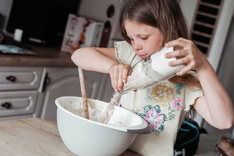 Child emptying Bottled Baking mix into mixing bowl