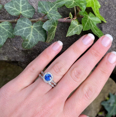 sapphire-halo-engagement-ring-with-diamond-wedding-band-on-hand-resting-on-rock