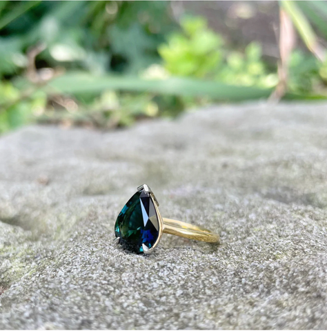  huge-teardrop-sapphire-ring-placed-on-rock-with-plants–in-background