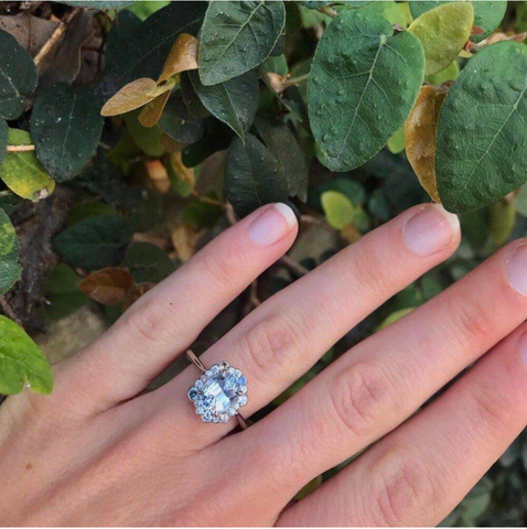 white-opal-engagement-ring-on-hand-in-front-of-plant-background