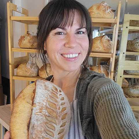 Stephanie in her cottage bakery holding up an artisan loaf