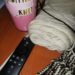 Knitters gonna knit cup with a knitting project, a fire stick  remote