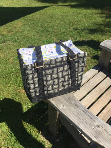 a fabric backpack lunch box in grey and lined in blue fabric sitting on an outdoor picnic table