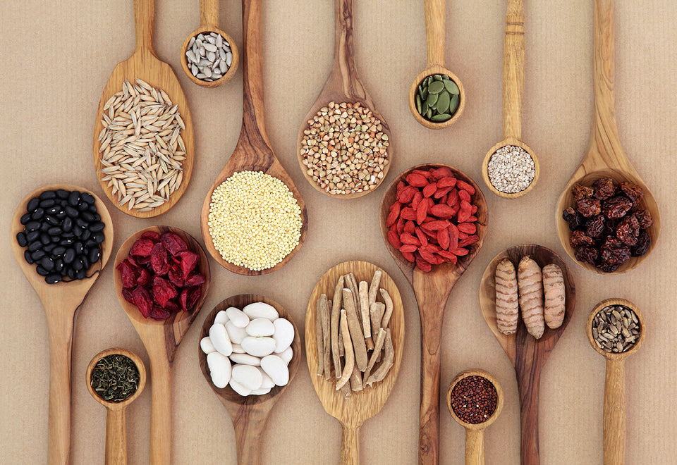 Various grains and legumes in wooden spoons on brown surface