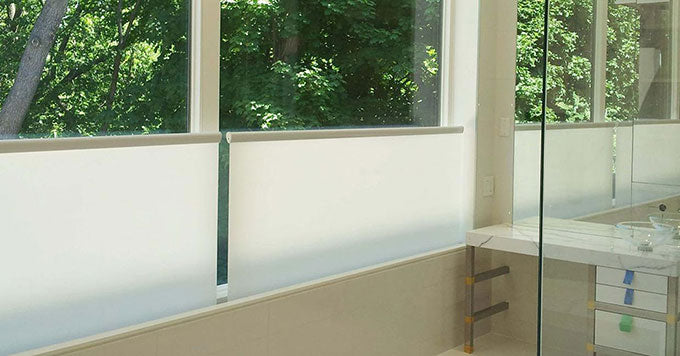 Altex bottom-up shades installed on the windows of a bathroom looking out onto a yard full of green trees