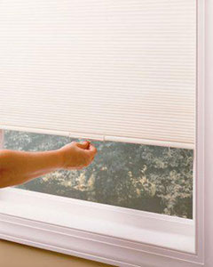a hand pulling down Elite cellular shades over a window in the day time